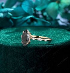 a black diamond ring sitting on top of a green velvet covered box with flowers in the background