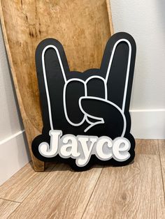 a wooden sign with the word jayce written in white on it and a hand holding a peace sign