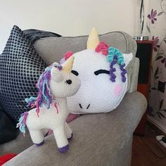 a crocheted stuffed unicorn sitting on top of a couch next to a pillow