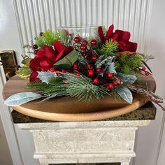 a wooden platter with red flowers and greenery on it sitting on a marble pedestal