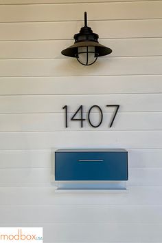 a house number sign mounted to the side of a wall with a lamp above it