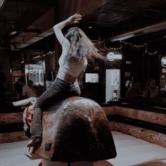 a woman riding on the back of a horse in a room with people sitting around