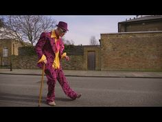 a man in a purple suit and hat is walking down the street with a cane