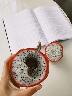 a person is holding a piece of fruit in front of an open book on a table