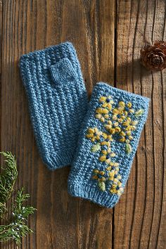 two blue knitted mittens sitting on top of a wooden table next to a pine cone