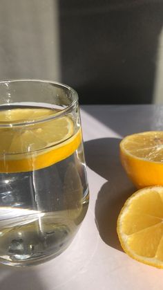 there is a glass of water with lemons on the table next to it,