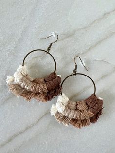 a pair of brown and white tasselled hoop earrings on a marble countertop