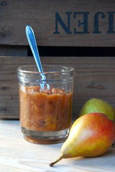 two pears are next to a jar of peanut butter on a wooden table with a blue spoon