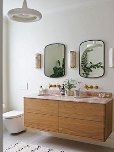 two mirrors on the wall in a bathroom with wooden cabinets and marble counter tops, along with potted plants