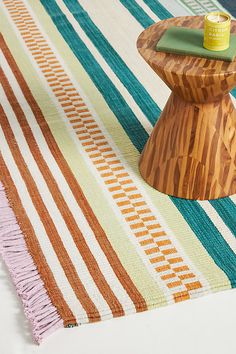 a small wooden table on top of a multicolored striped rug next to a candle