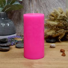 a pink candle sitting on top of a wooden table next to rocks and flowers in a vase