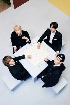 four young men sitting at a table with a board game in front of their faces