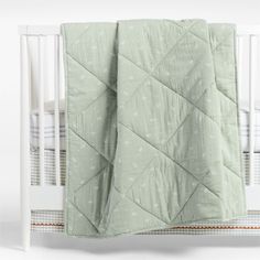 a baby crib with a green quilt on it's side and white bedding