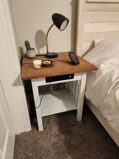 a small table with a lamp on it next to a bed