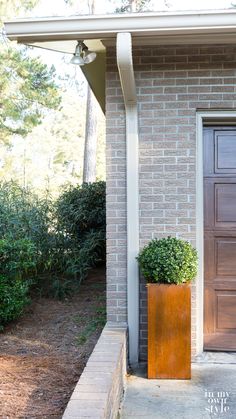 a tall planter sitting in front of a brick building next to a wooden door