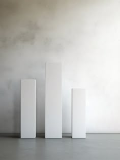 three tall white pedestals sitting in front of a wall