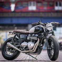 a black motorcycle parked on top of a brick road next to a red train track