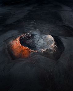 an orange and white crater in the middle of water with dark clouds above it at night