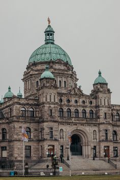 an old building with a green dome and two flags on the grass in front of it