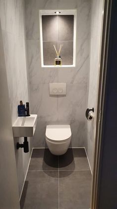 a white toilet sitting next to a sink in a bathroom under a window above a mirror