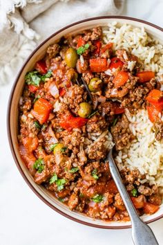 a bowl filled with meat and rice on top of a white tablecloth next to a spoon