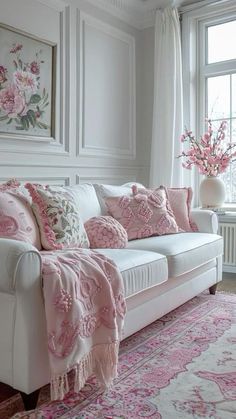 a white couch with pink pillows in front of a large window and rug on the floor