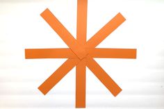 an orange piece of paper that has been cut into four intersecting pieces and is on top of a white surface