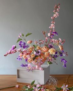 an arrangement of flowers in a white vase on a wooden table next to scissors and wire