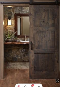 an open door leading to a bathroom with stone walls and wood floors, along with a sink