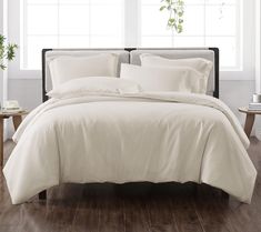 a bed with white linens and pillows in a room next to a plant on a table