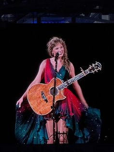 a woman in a dress holding a guitar on stage