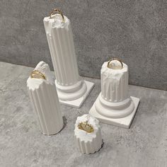 three white vases sitting on top of a cement floor next to two gold rings