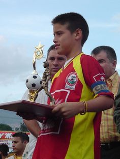 a young man holding a soccer trophy while standing next to other men