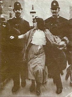 an old black and white photo of two women in gas masks being led by police officers