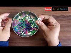 two hands holding a metal bowl filled with colorful beads