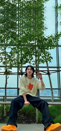 a young man sitting on top of a wooden bench next to a tall green tree