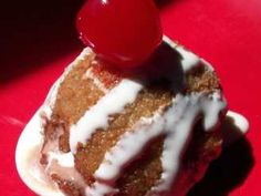 a piece of cake with white icing and a cherry on top is sitting on a red surface