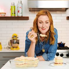 a woman sitting at a kitchen counter eating cake from a plate and holding a fork up to her mouth