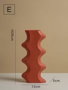 a tall red vase sitting on top of a white table next to a beige wall