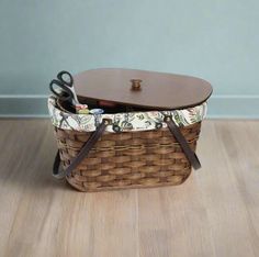 a brown basket with scissors and other items in it sitting on the floor next to a wall