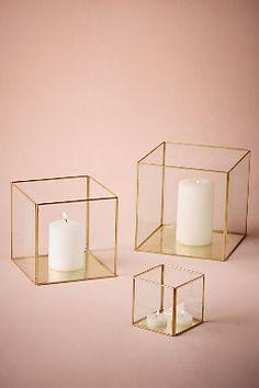 two glass boxes with candles inside on a pink background