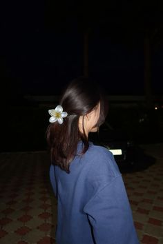 a woman with a flower in her hair looking down at the ground while wearing a blue sweatshirt