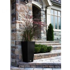 a tall black planter sitting on top of a stone walkway next to a building