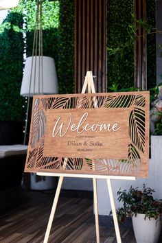 a wooden welcome sign sitting on top of a easel next to a potted plant