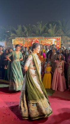 a woman in a green and white sari walking on a red carpet with other people