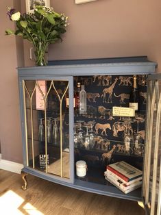 a blue china cabinet with glass doors and pictures on the wall behind it, in front of a vase filled with flowers