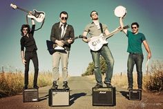 three men standing on top of guitars and amps in the middle of an empty road