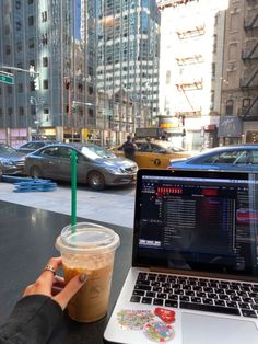 a laptop computer sitting on top of a table next to a cup of iced coffee