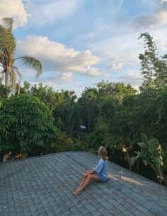 a woman sitting on top of a roof with trees in the background and clouds in the sky