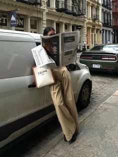 a man reading a newspaper while leaning against a car